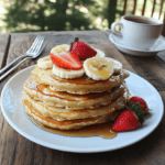 A stack of golden vegan banana pancakes topped with fresh fruit and maple syrup